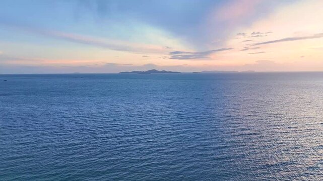 A scenic aerial view of Pattaya Bay at sunset with colorful orange and blue sky reflected on the calm sea and distant mountains visible.