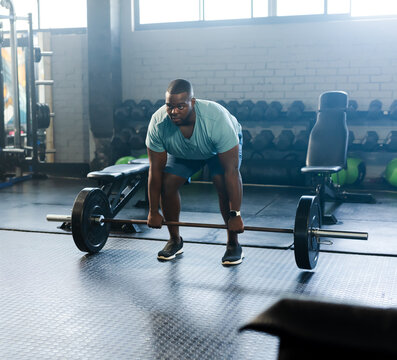 Muscular man performing deadlift with loaded barbell on rubber floor at gym near dumbbell rack