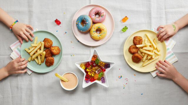 Children having fun sharing colorful party snacks together at a festive playdate table top view with children hands reaching reaching plates filled