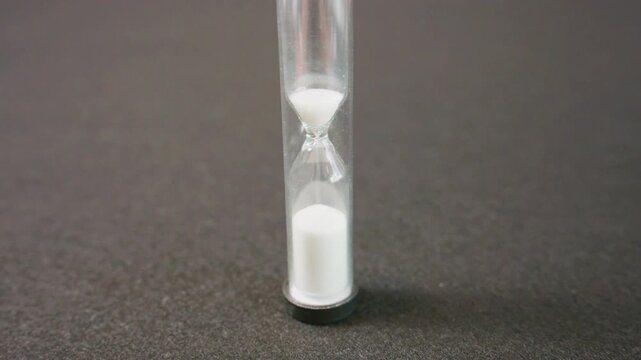 Small Glass Sand Timer With White Sand Running Down on Gray Surface