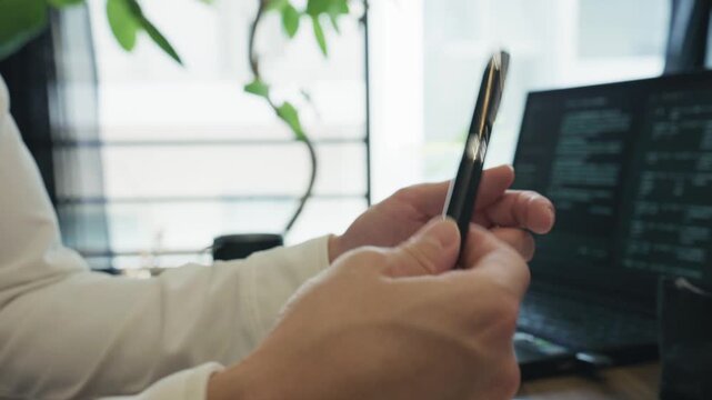 Close-up of hands turning a black pen between fingers beside a laptop with text on screen