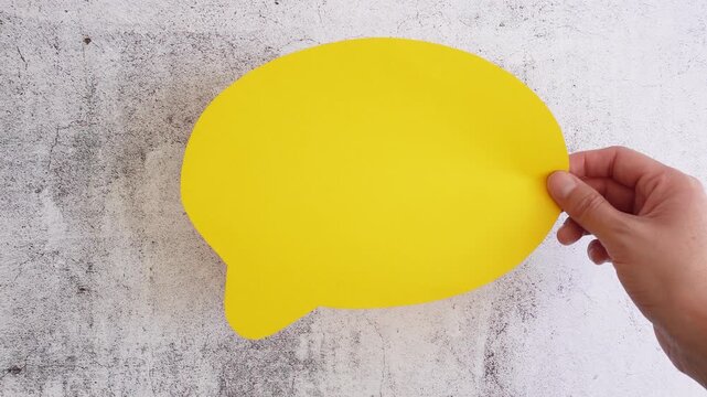 Hand presents a yellow speech bubble on a concrete surface