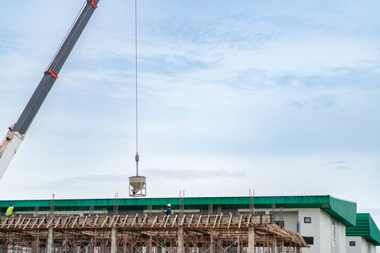 Crane hoisting a metal concrete bucket to transport liquid cement for building foundation and slab pouring work.