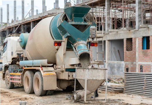 A concrete mixer truck discharging fresh wet concrete into a crane bucket at an active building construction site.