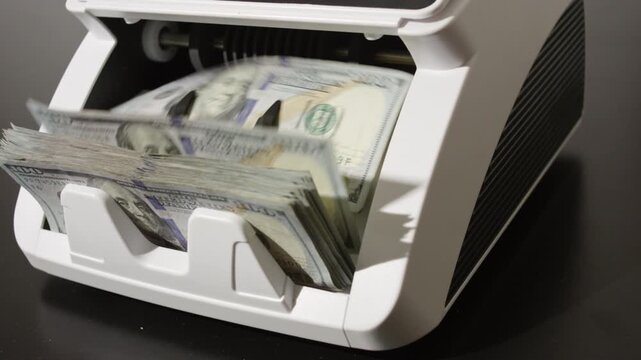 Money counting machine processing dollar bills in motion. Cash counting process with hundred dollar notes. Banking operation and finance concept with money movement. Counting machine working in bank