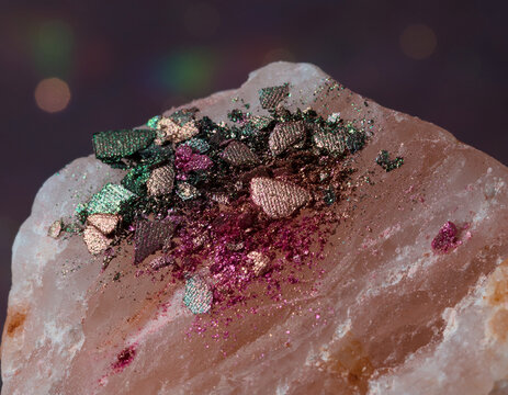 Crushed metallic green and magenta eyeshadow pigments resting on raw stone.