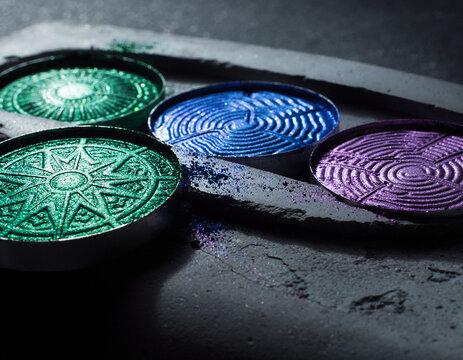 Multi-chrome eyeshadow pans with intricate embossed geometric patterns on textured stone