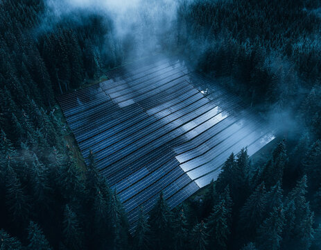 Aerial view of solar panel array installed in a clearing surrounded by a dense misty forest