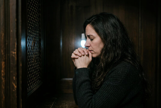 Devout woman praying intently inside a dark wooden confessional booth
