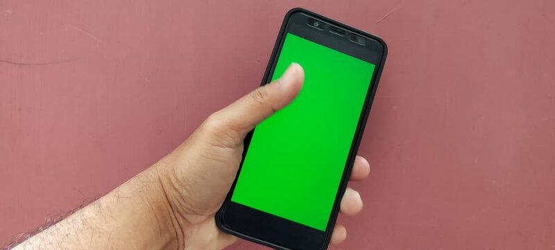 Hand holding a smartphone with a green screen background.