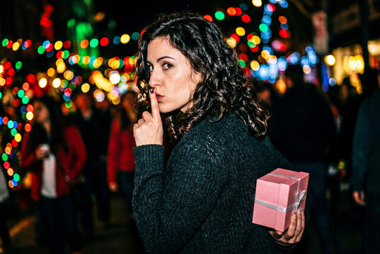 Woman holding secret pink gift box at night during holiday festival