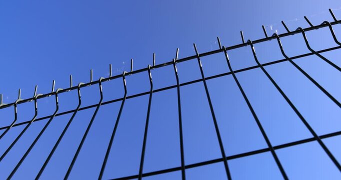 Black steel wire fence under bright blue sky, metal mesh fencing grid enclosing private area or restricted property territory outdoors