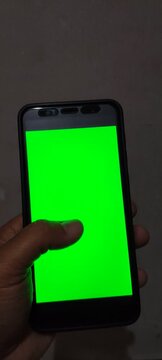 Close up of hand holding smartphone with green screen in landscape mode.