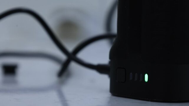 A close-up of a black portable power bank with blue LED indicator lights and charging cables on a desk surface.
