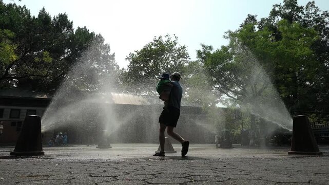 alt slow motion summer man carries child through sprinklers in Brooklyn park