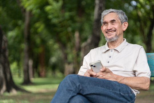 portrait elderly pensioner man spend leisure time relaxing in urban park,sitting on bench,holding mobile phone,smiling and looking in nature