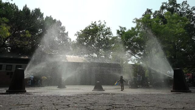 slow motion summer boy with pail plays in sprinklers in Brooklyn park
