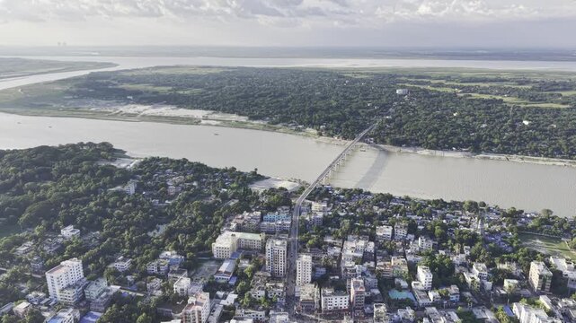 Aerial drone footage showing Kushtia city in Bangladesh, with small and large buildings, residential areas, abundant green trees, and a blue sky with scattered white clouds.