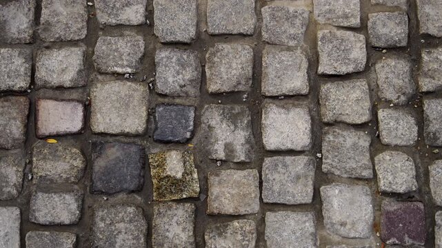 Top down aerial shot moving forward over an ancient rough cobbled stone pavement street with small rectangular unpolished cobbles.