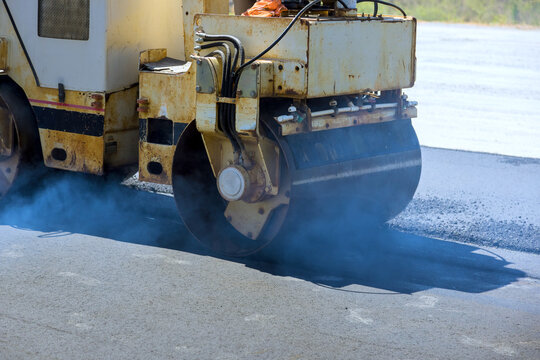 Construction work is taking place as steamroller compacts asphalt on road surface
