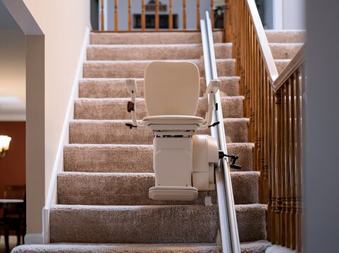 Stair lift chair parked at the bottom of a residential carpeted staircase in a warm home interior