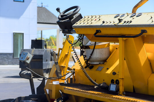 Construction paving machine is parked near building with tools visible on dashboard