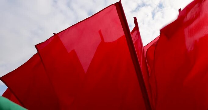 Bright red flags against a cloudy sky, large red flags flutter on flagpoles outdoors during a public event