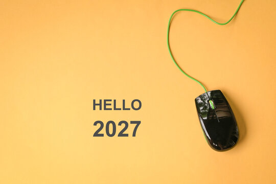 Hello 2027, message next to computer mouse, on top of yellow surface. Top view.