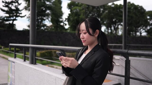 丸の内の歩道でスマートフォンを見る若い若いビジネスウーマン
