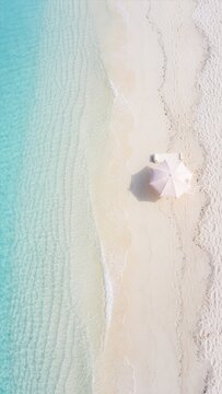 エメラルドグリーンの透明な海と白い砂浜に置かれた日よけパラソルとビーチベッドの俯瞰　縦長構図