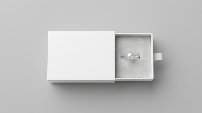 A white sliding jewelry box partially open revealing a silver ring with a white pearl inside on a soft gray background, for product display