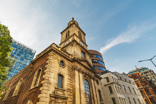 View of St. Magnus the Martyr church with its historic clock tower and stone facade set against modern glass buildings in London, England, United Kingdom.