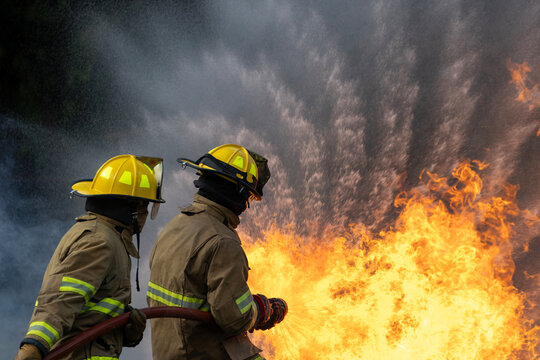 Team of firefighter in fireproof clothe are using twirl fog watering hose to put out the burning building with high flame for fire extinguish risk rescue mission, accident management