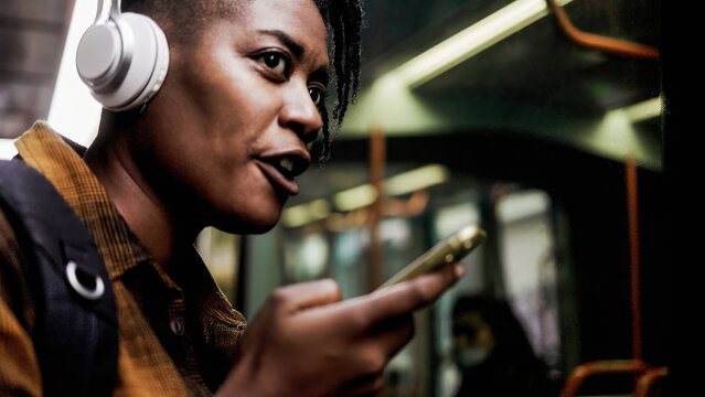 Black woman using smartphone at bus station - African girl sending voice on mobile phone - Focus on face