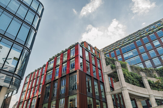 View of modern office buildings with glass facades, red metal accents, and vertical gardens in the City of London, England, United Kingdom.