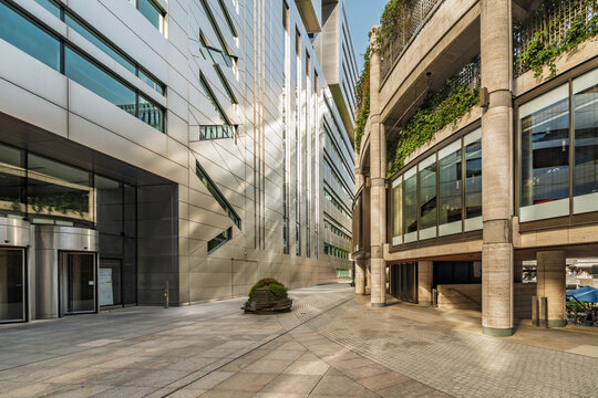 View of modern architecture with a sleek metallic facade and concrete pillars featuring green balconies along a paved walkway in the City of London, London, England, United Kingdom.