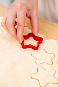 Cooking sweets. Festive pastry recipe. Baker female hand making star shape white cookies on wooden countertop from flour dough sheet.