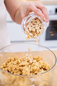 Baking process. Peanut pastry. Woman chef hand pouring peanut in bowl with yellow dough preparing tasty meal recipe in home kitchen.