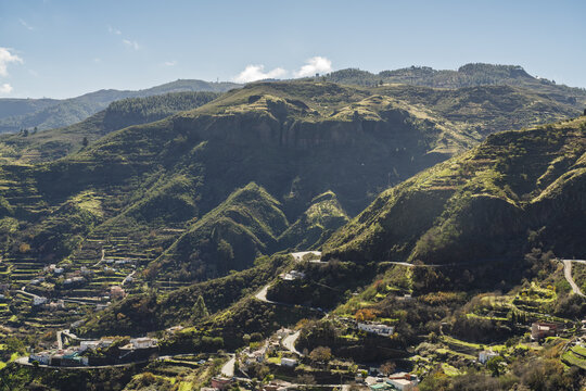 View of the mountainous landscape with terraced hillsides, winding roads, and scattered houses under a clear blue sky in Vega de San Mateo, Canary Islands, Spain.
