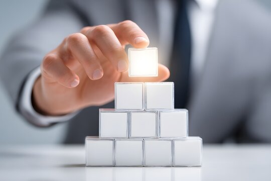 Hand placing illuminated cube atop stacked blocks to complete business structure