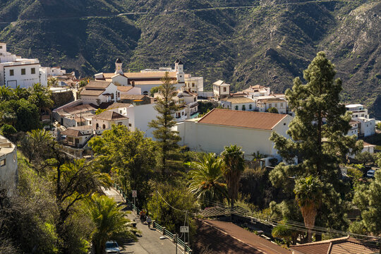 View of the village of Tejeda nestled in the mountainous landscape of the Canary Islands, with white buildings, a church, and lush greenery under a clear sky, Tejeda, Canary Islands, Spain.