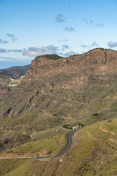 View of a winding mountain road through the rugged landscape with rocky slopes and sparse vegetation in Tejeda, Canary Islands, Spain.