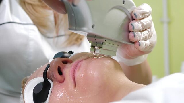 Professional skincare expert in transparent gloves applying intense pulsed light device over wet face. Safety glasses protect eyes, intensive anti-aging collagen stimulation procedure, vertical 4k