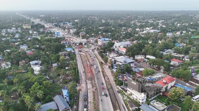 Wide aerial panorama of the Cochin Highway in Ambalappuzha featuring a flyover construction project, heavy traffic, urban settlements, and lush green surroundings.