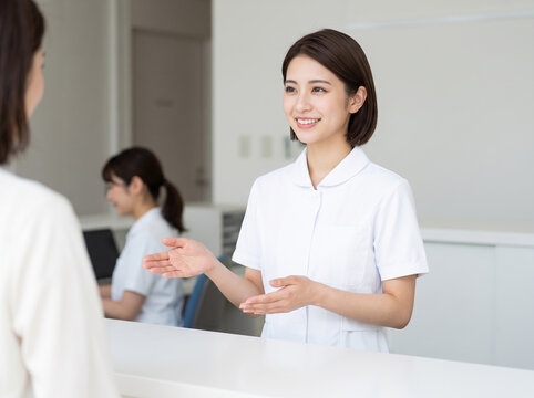 来院者と会話を交わしながら案内板を指し示す受付担当の事務スタッフ