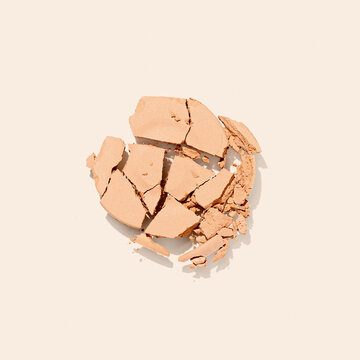 Single crumbled eyeshadow, foundation powder swatch in light brown tones on beige background. Broken powder texture, natural nude beauty and makeup design minimal concept. Monochrome beauty photo.
