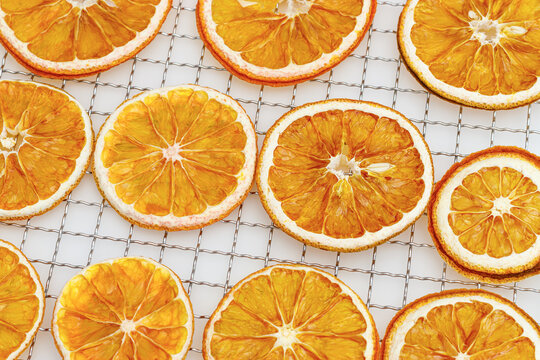 Natural dried oranges on grid for dryer on white background. Sliced and dried candied citrus fruit food pattern. Minimal top view aesthetic still life of aromatic vivid yellow round orange pieces.