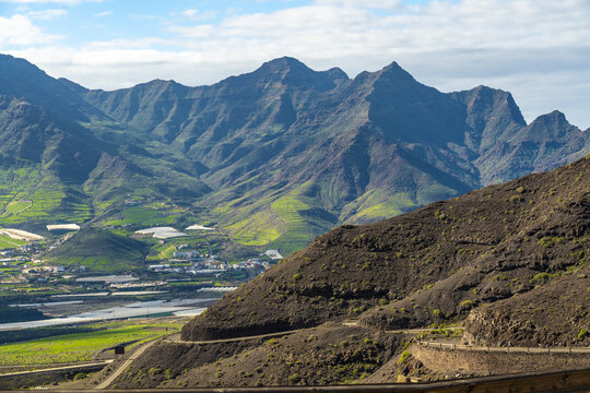 View of La Aldea de San Nicolas featuring dramatic volcanic mountains, lush green terraced fields, and a winding road in Las Palmas de Gran Canaria, Canary Islands, Spain.