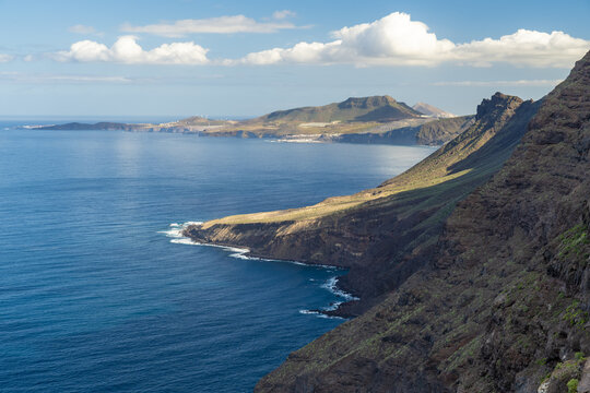 View of the dramatic coastal cliffs of La Aldea de San Nicolas rising above the deep blue Atlantic Ocean under a bright sky in Las Palmas de Gran Canaria, Canary Islands, Spain.