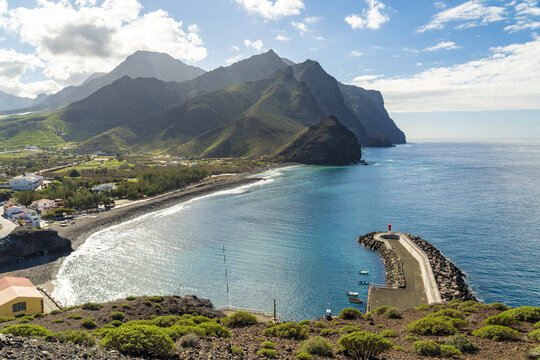 View of the coastal landscape at La Aldea de San Nicolas with a small harbor, boats, and dramatic mountains meeting the blue sea in Las Palmas de Gran Canaria, Canary Islands, Spain.